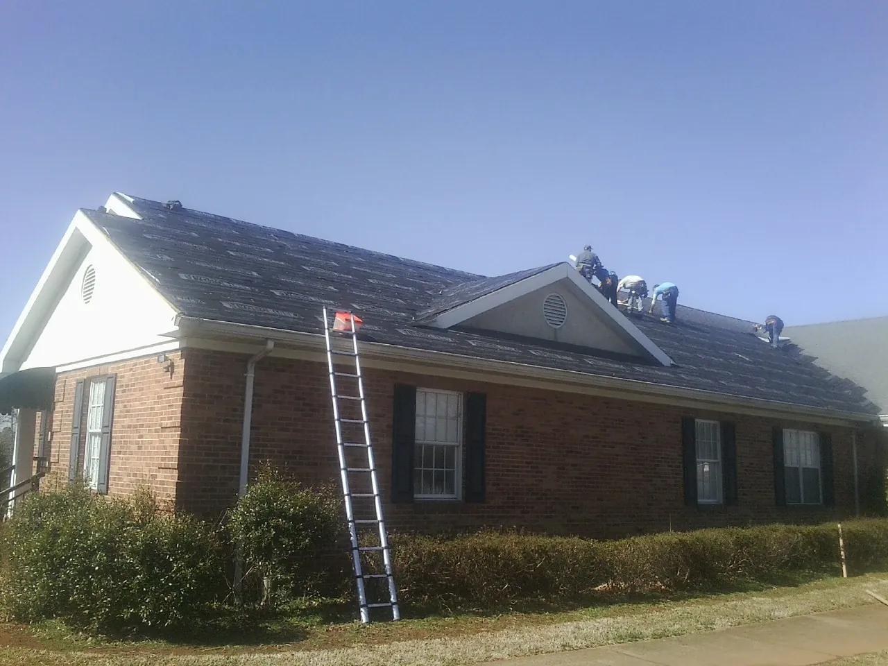 Crew tearing shingles off a brick ranch roof with a ladder set — Emergency Roof Repair work by our crew in Orion