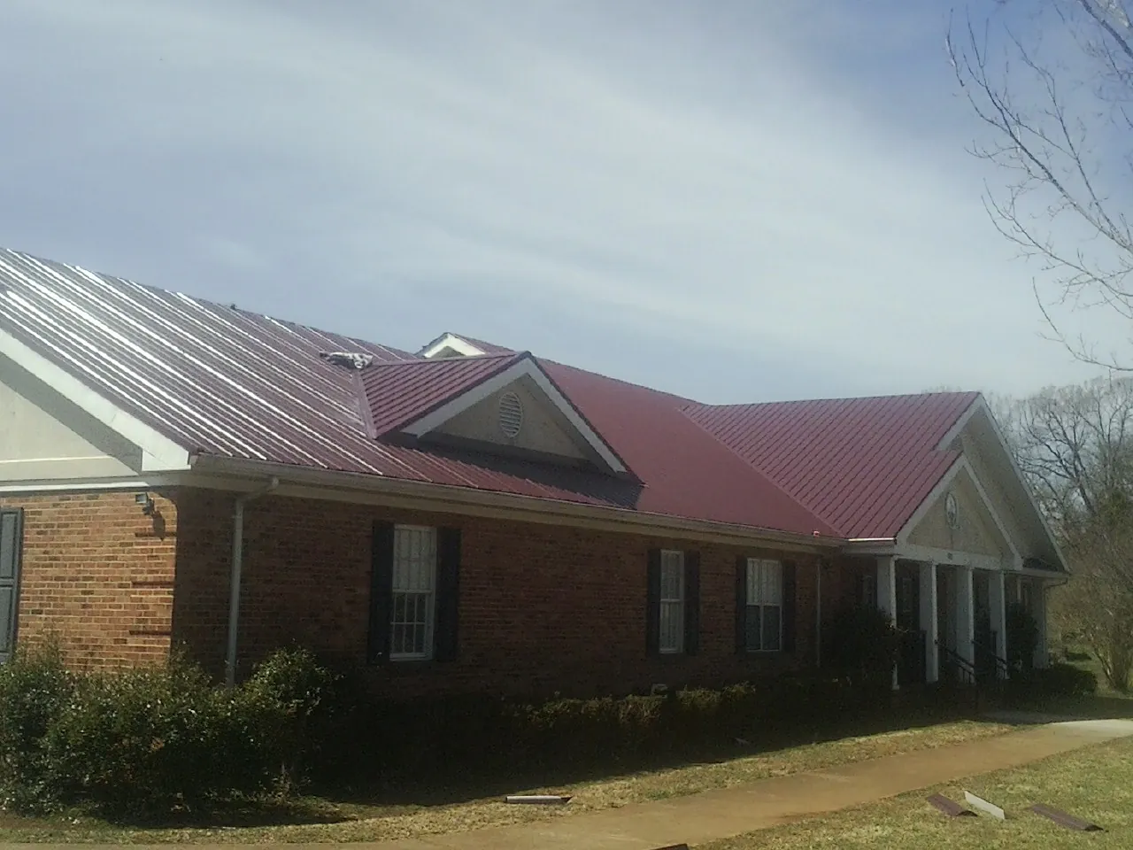 Red metal roof with gabled entries on a long brick building, from a Hail Damage Roof Repair job in Orion