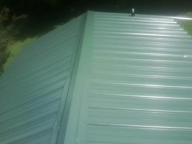 New green metal panels meeting at the ridge of a roof — Flat Roof Repair work by our crew in Orion