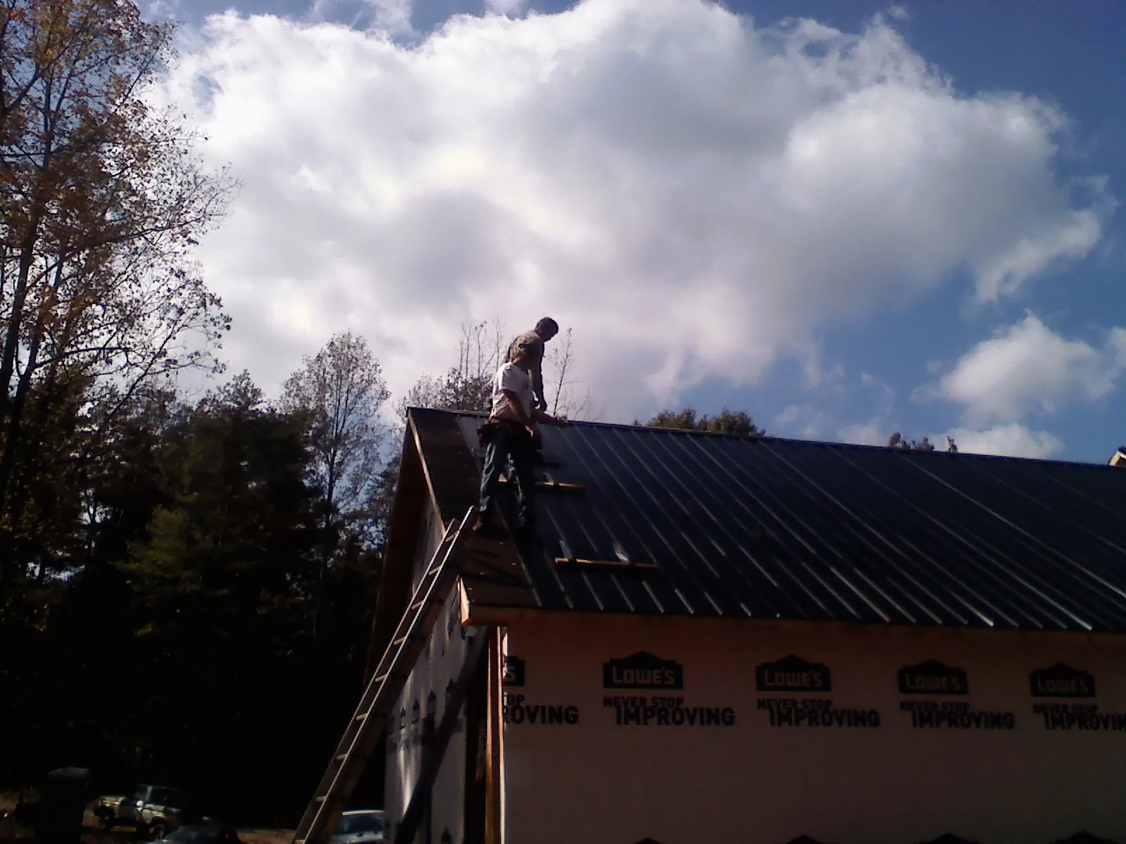 Roofer fastening dark metal panels high against a cloudy sky, from a Roof Inspection job in Orion