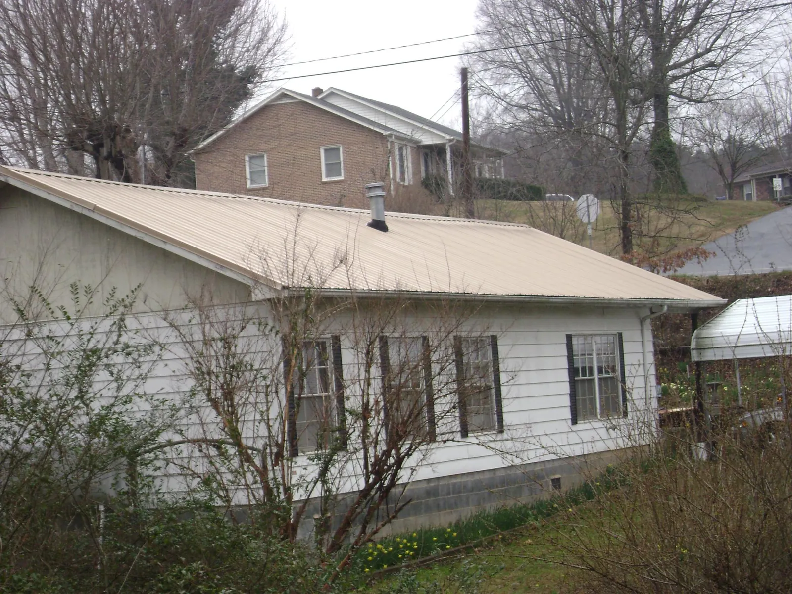 Tan metal roof on a white sided house set into a hillside — Commercial Roofing by Roofing Brothers in Orion